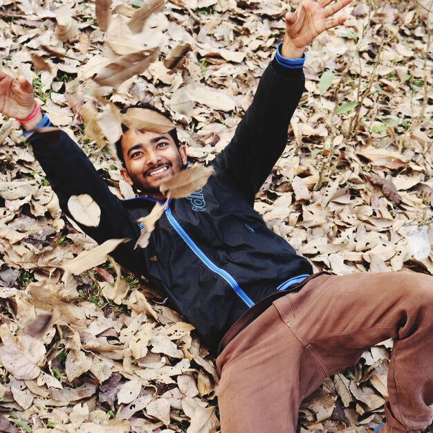 Foto hombre sonriente acostado en tierra mientras juega con la hoja de otoño