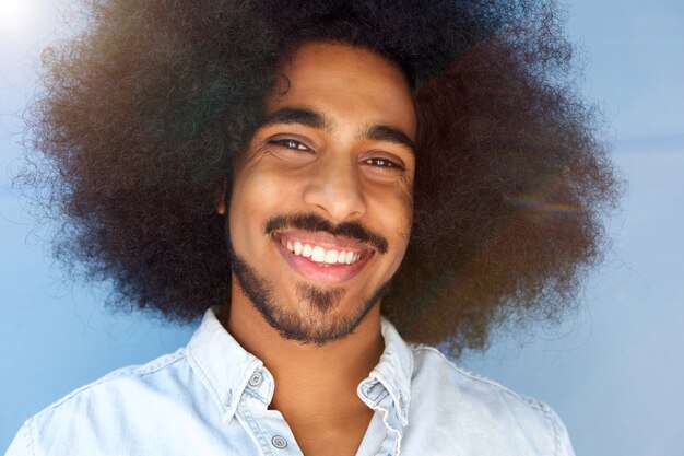 Hombre sonriente con afro y barba por la pared azul