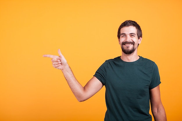 Hombre sonriente alegre apuntando a su derecha en copyspace disponible para su publicidad o promoción. Aislado sobre fondo naranja en estudio.