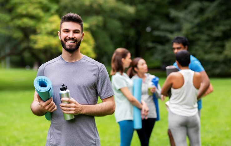 Foto hombre sonriente con una alfombra de yoga sobre un grupo de personas