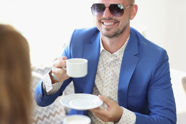 Hombre sonriente bien vestido tomando café en la cafetería en una reunión de negocios con un socio