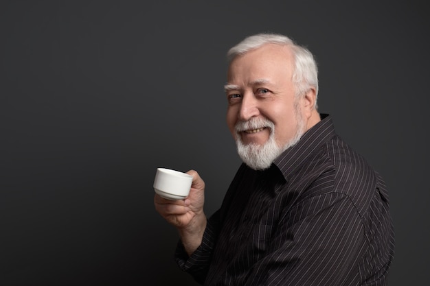 El hombre sonriente bondadoso que sostiene una taza y mira en el marco