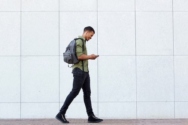 Foto hombre sonriente caminando con mochila teléfono inteligente y auriculares