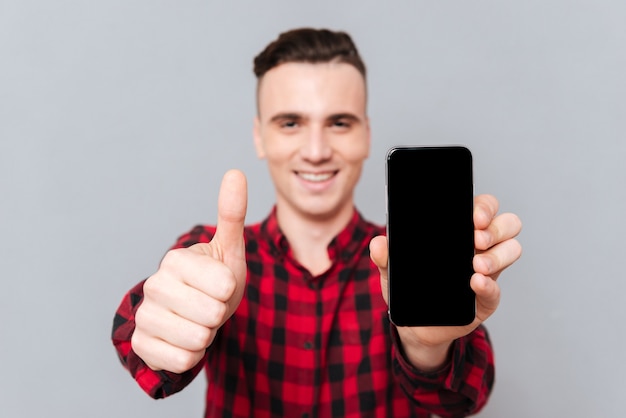 Hombre sonriente con camisa roja que muestra la pantalla del teléfono inteligente en blanco y mostrando los pulgares para arriba.