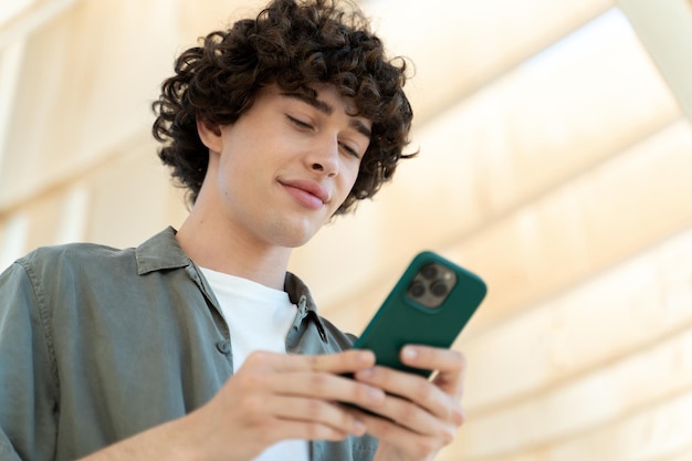 Hombre sonriente con camisa verde usando teléfono móvil en la calle de la ciudad