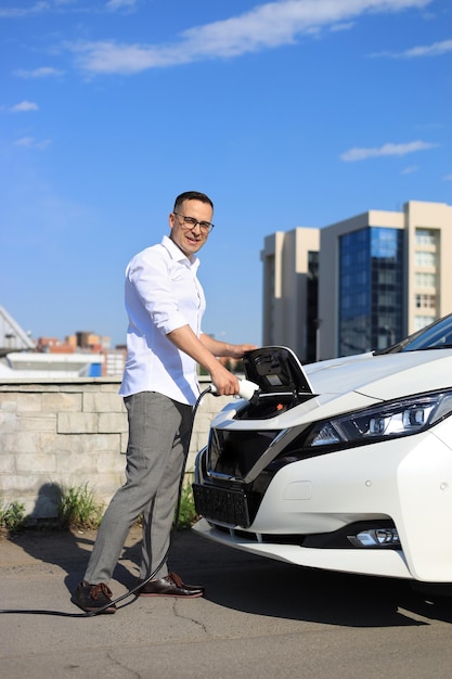 Hombre sonriente cargando coche eléctrico en energía verde y concepto de energía ecológica destinado a reducir las emisiones de CO2