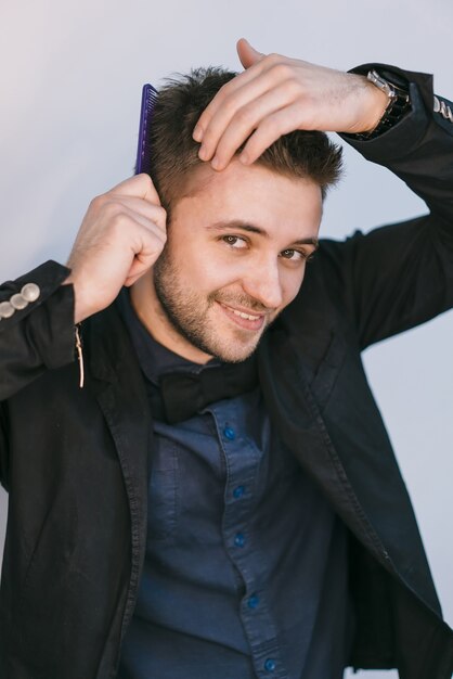 Foto un hombre sonriente con una chaqueta negra peina su cabello con un peine en el estudio.