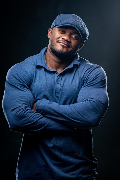 Hombre sonriente confiado tiene las manos cruzadas. Foto de hombre africano en ropa casual sobre fondo negro.