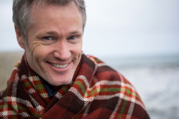 Hombre sonriente envuelto en un chal en la playa