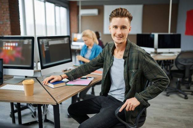 Hombre sonriente especialista en TI se sienta a la mesa en la oficina. Programador web o diseñador en el lugar de trabajo, ocupación creativa. Tecnología de la información moderna, equipo corporativo.