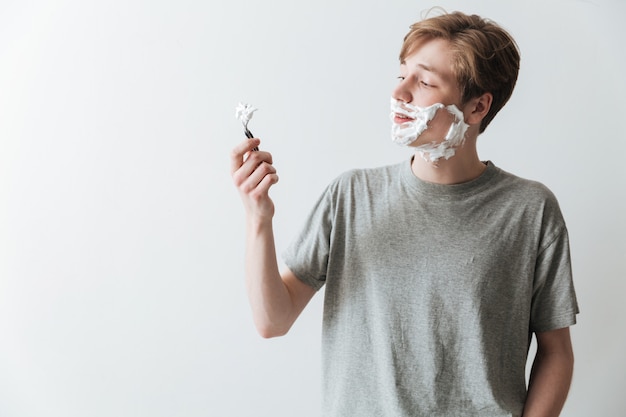 Hombre sonriente en espuma de afeitar mirando la maquinilla de afeitar