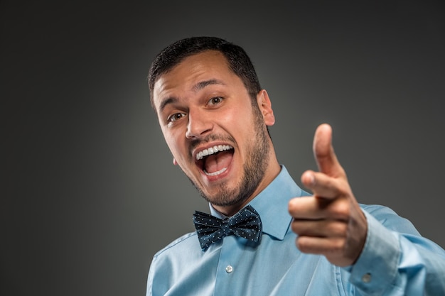 Hombre sonriente está gesticulando con la mano, apuntando con el dedo a la cámara