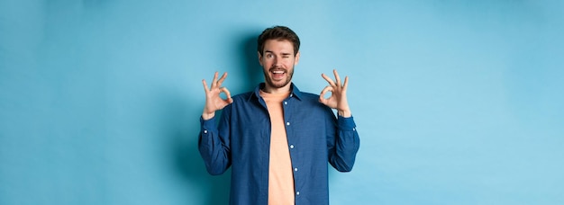 Foto hombre sonriente feliz guiñando un ojo y mostrando bien ok signo decir sí aprobar y estar de acuerdo con algo bueno st