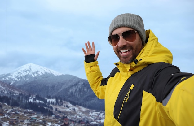 Hombre sonriente con gafas de sol tomando selfie en las montañas