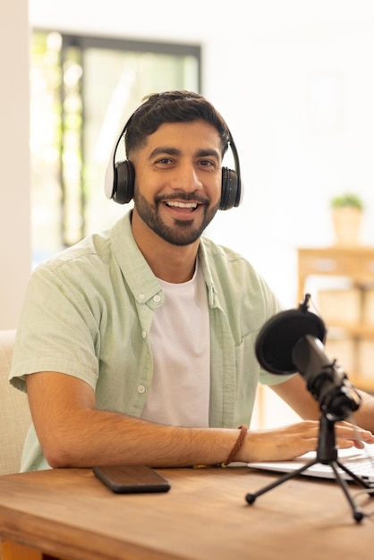 Hombre sonriente grabando podcast con micrófono y auriculares en su oficina en casa