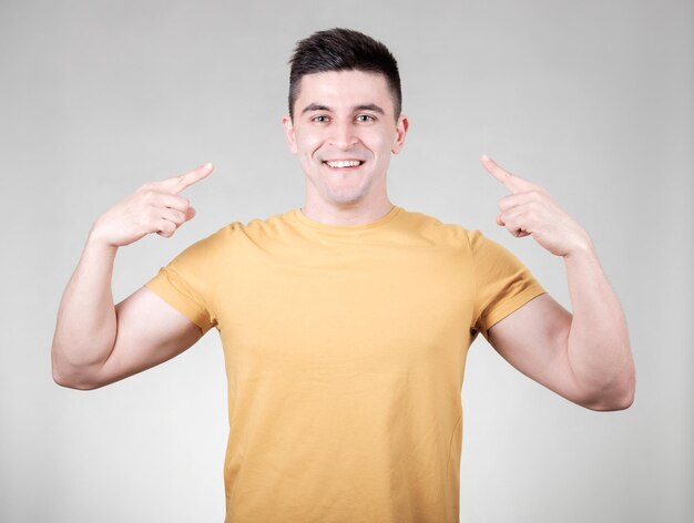 Un hombre sonriente y guapo apuntándose a sí mismos aislados sobre fondo gris