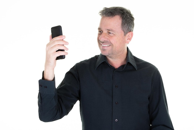 Hombre sonriente guapo haciendo selfie smartphone con teléfono celular sobre fondo blanco.