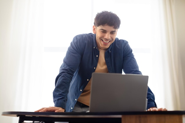 Un hombre sonriente y guapo del Medio Oriente trabajando con una computadora portátil en el lugar de trabajo