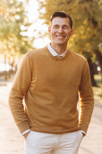 Hombre sonriente guapo moderno en ropa amarilla y blanca posando en el parque al atardecer