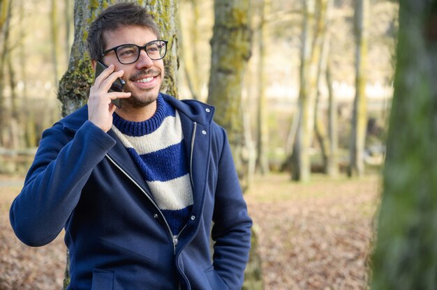 Hombre sonriente, hablando por teléfono móvil en un parque de otoño.