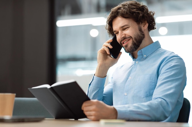 Hombre sonriente hablando por teléfono en la oficina leyendo diario