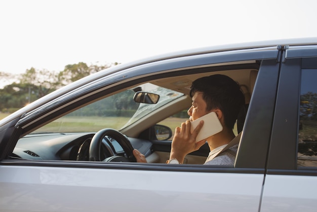 Foto hombre sonriente hablar por teléfono inteligente en coche blanco. el empresario exitoso conduciendo su automóvil y hablando por teléfono celular.