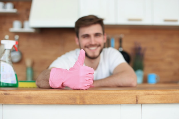 Foto hombre sonriente hermoso joven que limpia la cocina moderna.