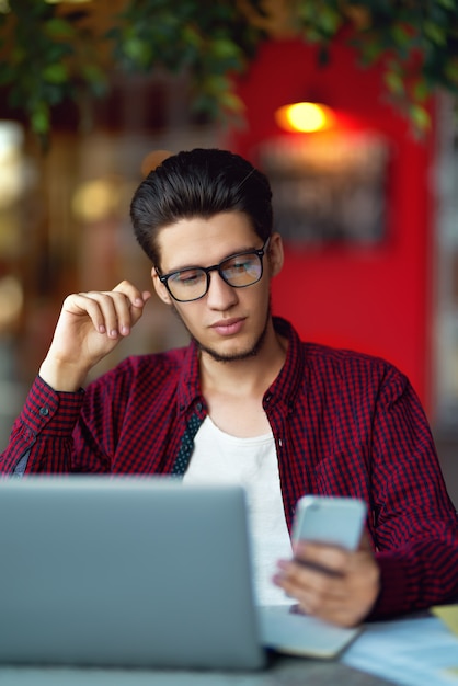 Hombre sonriente joven inconformista en vasos con el portátil sobre la mesa. Programador, desarrollador web, diseñador que trabaja en la oficina.