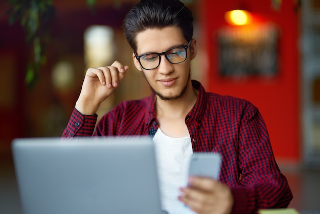 Hombre sonriente joven inconformista en vasos con el portátil sobre la mesa. Programador, desarrollador web, diseñador que trabaja en la oficina.