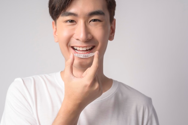 Hombre sonriente joven que sostiene las llaves de Invisalign sobre el estudio dental del fondo blanco