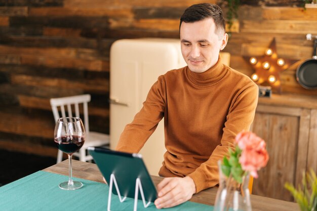 Hombre sonriente joven que usa la computadora de la tableta que tiene videochat en línea con los amigos