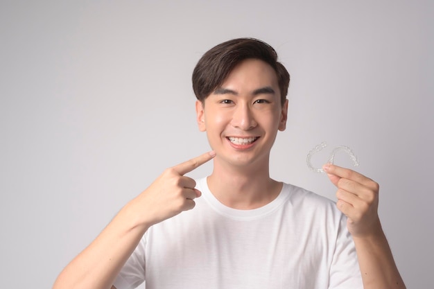 Hombre sonriente joven sosteniendo aparatos ortopédicos invisalign sobre estudio de fondo blanco