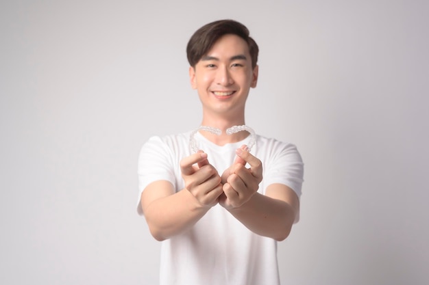 Hombre sonriente joven sosteniendo aparatos ortopédicos invisalign sobre estudio de fondo blanco