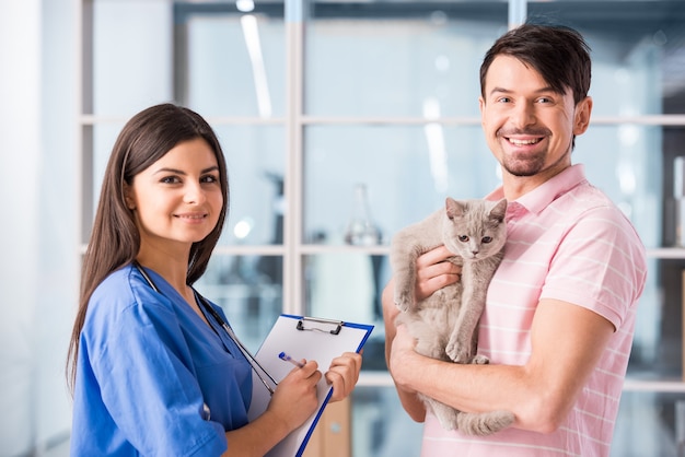 Hombre sonriente joven con su gato lindo en una visita al veterinario.