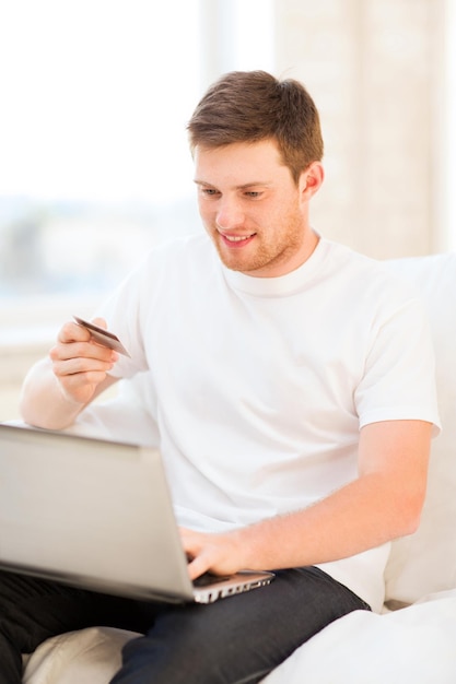 Hombre sonriente con laptop y tarjeta de crédito en casa