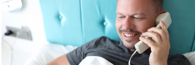 Hombre sonriente llamando a la recepción en el hotel quiere pedir el almuerzo en la habitación