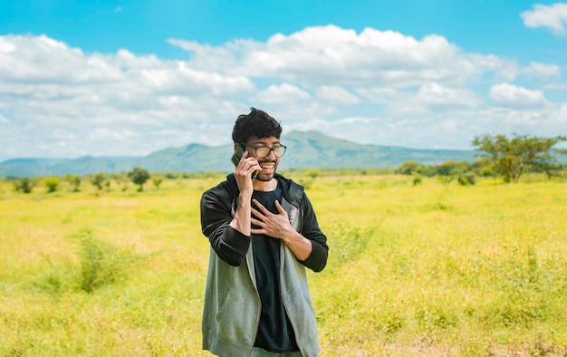 Hombre sonriente llamando por teléfono en el campo gente hablando por teléfono celular en el campo Hombre llamando por teléfono en el campo Un hombre en un hermoso campo hablando por teléfono