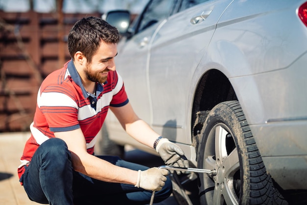 Hombre sonriente y mecánico cambiando neumáticos usando gato y llave de rueda