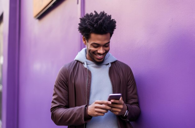 un hombre sonriente mirando su teléfono mientras está de pie en una pared de la calle púrpura