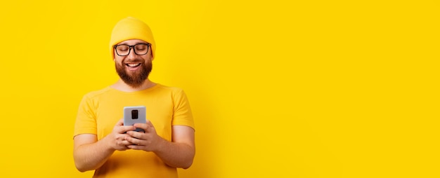 Hombre sonriente mirando el teléfono sobre fondo amarillo, diseño panorámico