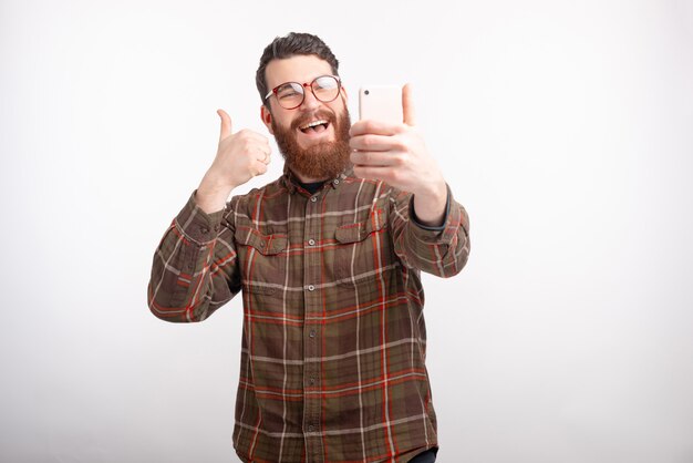 Foto el hombre sonriente está mostrando el pulgar hacia arriba está haciendo un selfie sobre fondo blanco.