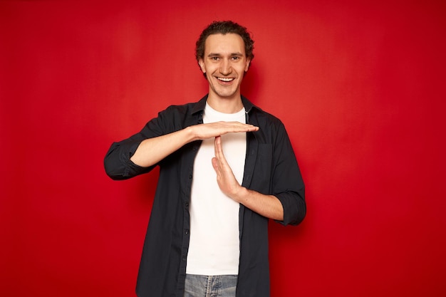 Hombre sonriente muestra gesto de tiempo de espera necesita detener pide tiempo para descansar espacio de copia de fondo rojo aislado