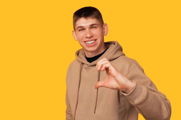 Un hombre sonriente muestra la mitad de un gesto de corazón sobre un fondo amarillo