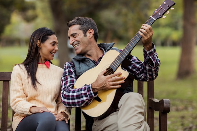 Hombre sonriente con mujer tocando la guitarra en el banco