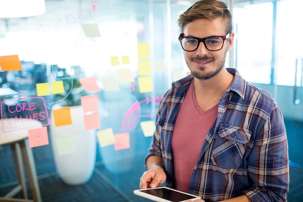 Hombre sonriente en la oficina con tableta digital contra notas adhesivas en la pared