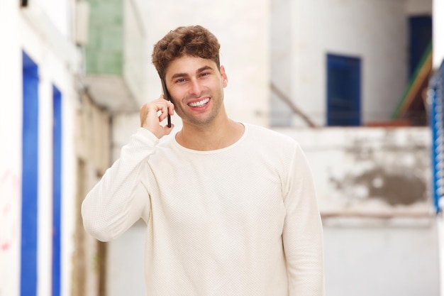 Hombre sonriente de pie en la calle de la ciudad hablando por teléfono móvil