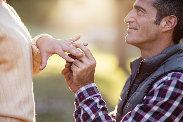 Hombre sonriente poniendo anillo en mano de mujer