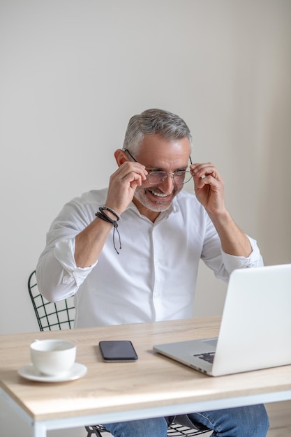 Hombre sonriente poniéndose anteojos mirando la computadora portátil