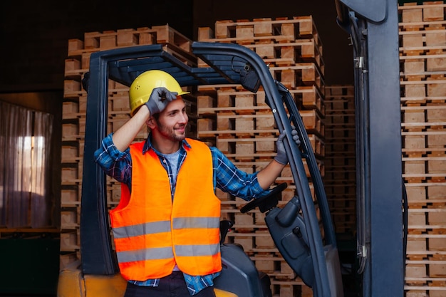 Foto hombre sonriente posando cerca de la carretilla elevadora apiladora industrial en el almacén