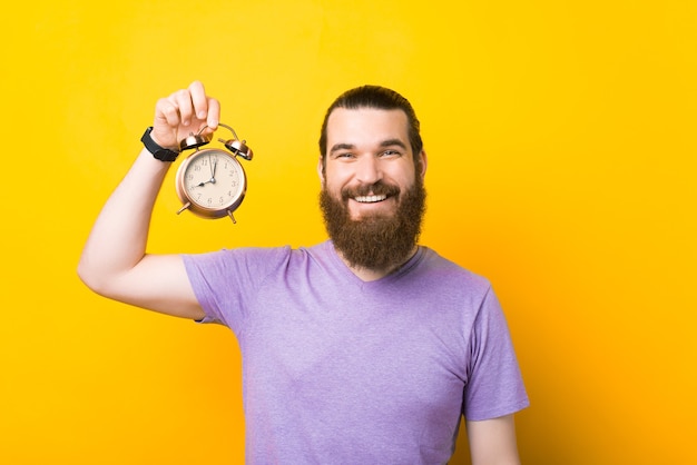 El hombre sonriente positivo está sosteniendo un reloj de alarma.